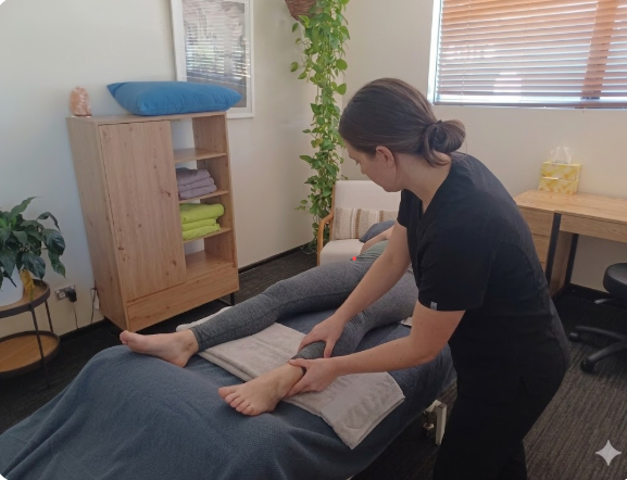 A professional female therapist performs a targeted clinical massage on a client's ankle and lower leg to improve mobility and reduce localized tension.