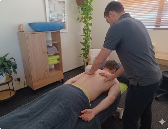 A professional male therapist applies firm, clinical pressure to a client's upper back and shoulder blades during a remedial massage session to help alleviate tension and improve posture.