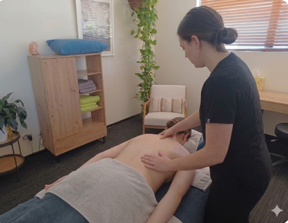 A professional female therapist applies clinical massage techniques to a client's back and neck in a calm, modern treatment room to help reduce stress and muscle stiffness.
